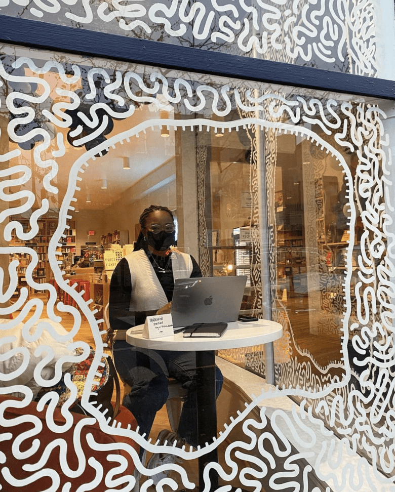 A woman uses a laptop at the White Whale Bookstore. atiya jones' artwork is painted on the window's glass.