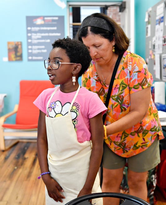 Local artist and art therapist Rosa Luz Catterall, back, helps Irisa Zitrick, 7, of Mount Wolf, with an apron while leading a monthly art wellness activity at Marketview Arts in York City, Saturday, July 6, 2024. (Dawn J. Sagert/The York Dispatch)