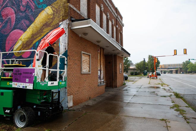 As a freight train passes in the distance, San Francisco native Cameron Moberg takes a break from spray painting the Monarch Building at 519 S. Michigan St. to see if he spots any of his friends' graffiti on Friday, July 5, 2024, in South Bend. Moberg says during mural festivals, it is easy to spot who is a graffiti artist, as they will stop and watch passing freight trains.