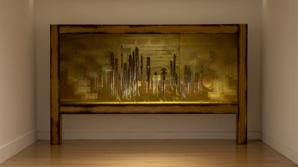 A large rectangular artwork by Seattle artist Mary Ann Peters displayed at the Frye Gallery features a mix of vertical and abstract shapes with a golden-yellow color palette. The floor is wooden, and the walls are plain.