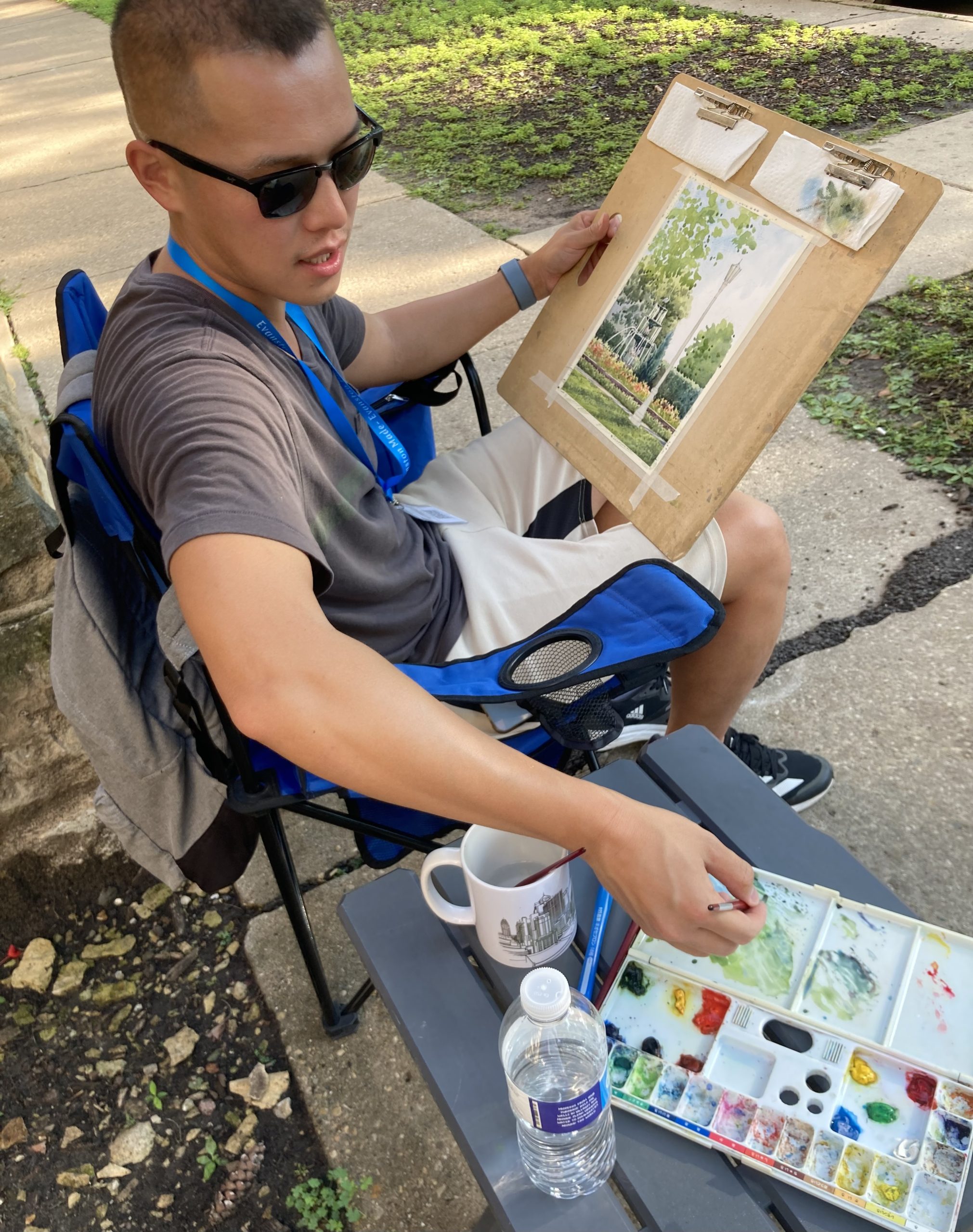 seated young man with sunglasses, painting on small drawing board