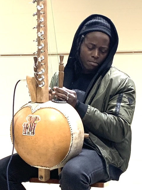 young, hooded black man playing an African stringed intrument