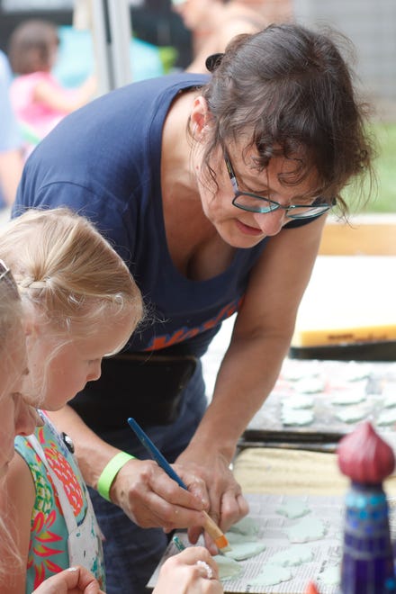 Local artist Krysia Ara works with a child to glaze ginkgo leaves that will used in her mosaics at FoxSaid Festival at the Cotton Press in Athens, Ga., on Saturday, July 27, 2024. The art and music festival featured interactive art with a number of local artists and raised money for art education in local schools.