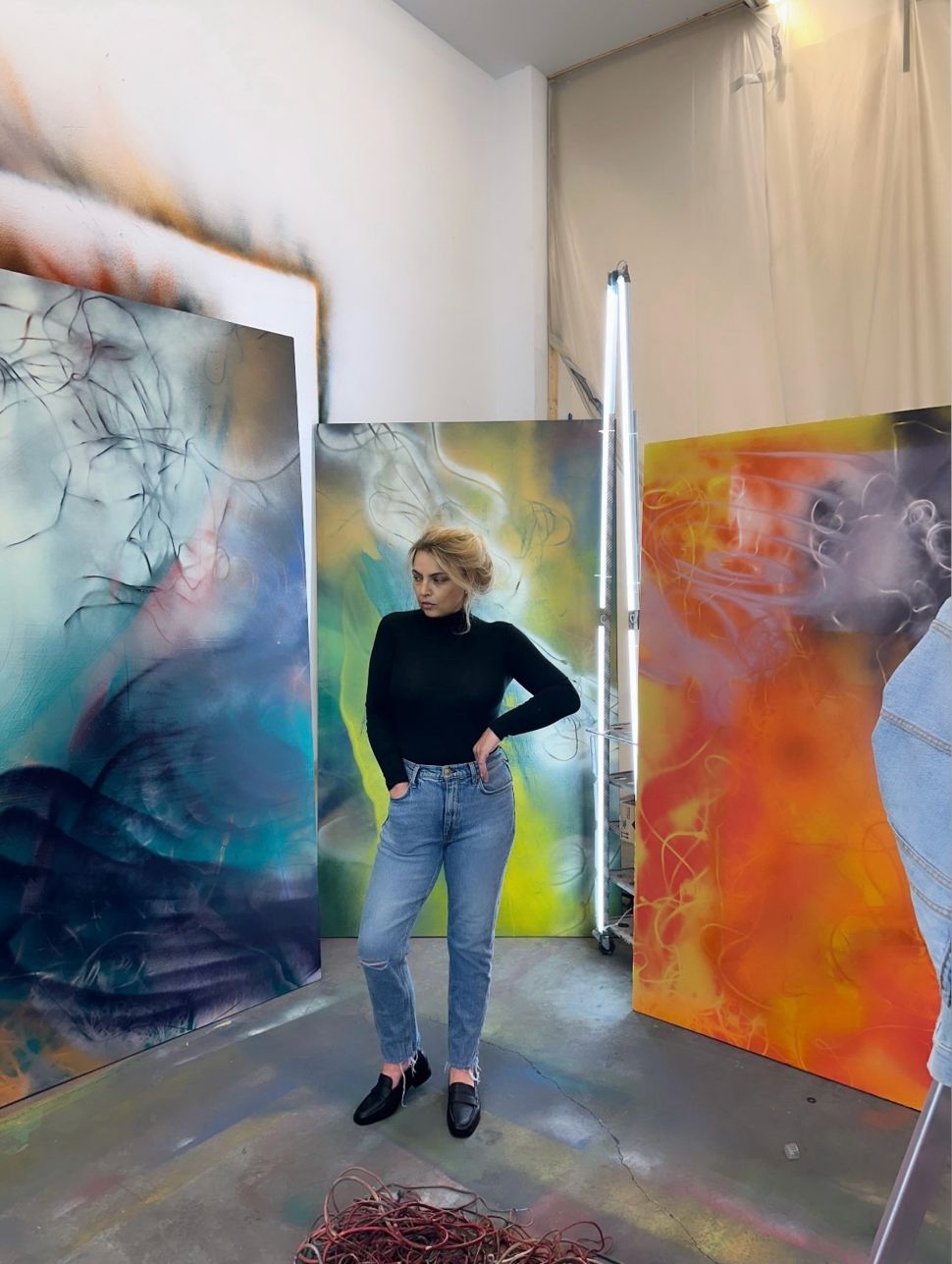 Photo of a blonde girl in the studio with colorful abstract pantings