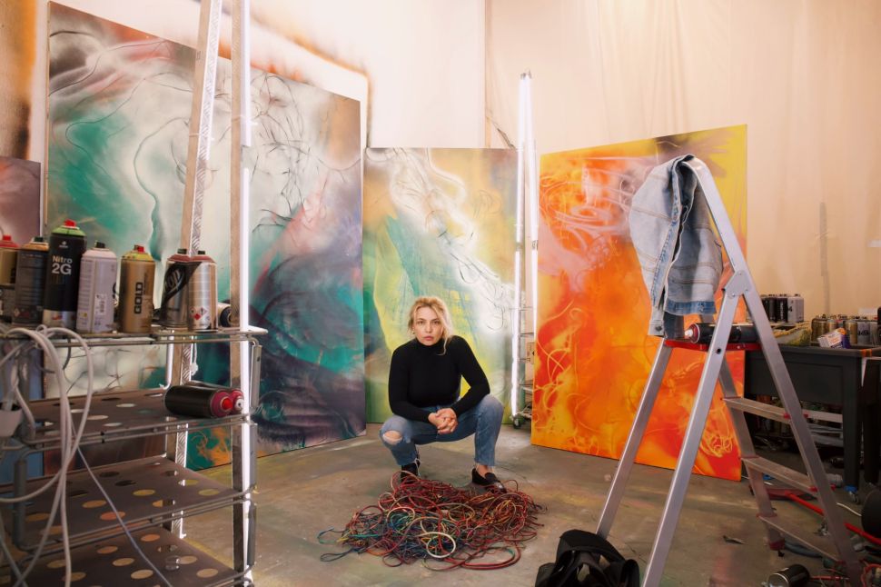 Photo of a blonde girl in the studio with colorful abstract pantings