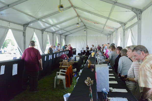 Bidders walk around a silent auction table featuring smaller, less-expensive sculptures during Saturday's Sculpture in the Park show. (Riley Laub / Loveland Reporter-Herald)