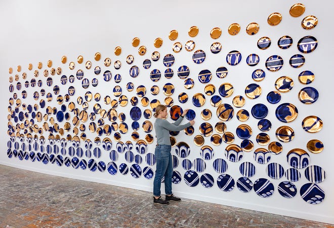 Artist Molly Hatch places ceramic plates as part of her exhibition of “Amalgam” at the Sarasota Art Museum.