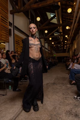 A model shows off their torso tattoos and wears a long lace skirt.