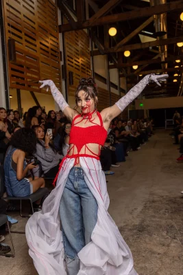 A model wearing a red corset and a pink tulle skirt around their jeans strikes a pose.