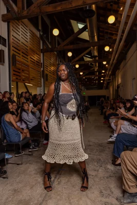 A model poses in a tan crocheted, fitted dress.