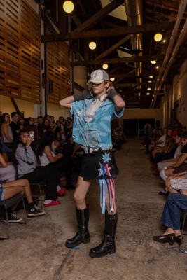 A model wears a bright blue top, tall boots and a trucker hat.