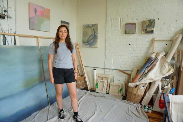 a woman stands in front of a large canvas and other art supplies.