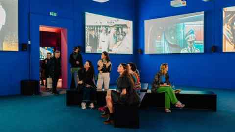 A group of people, mainly young women, inside a blue-walled art gallery with large pictures on its walls