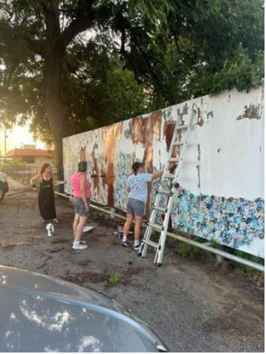 Denton artist Camille Green, left, rolls fresh paint onto the south-facing wall at Denton Discount Vacuum on Locust Street. Painters Kiba Jacobson, right, and Marie Goodwyn, center, prepare to put a new mural on the building. North Texas Mural Co. is a new company that is painting murals across the country.